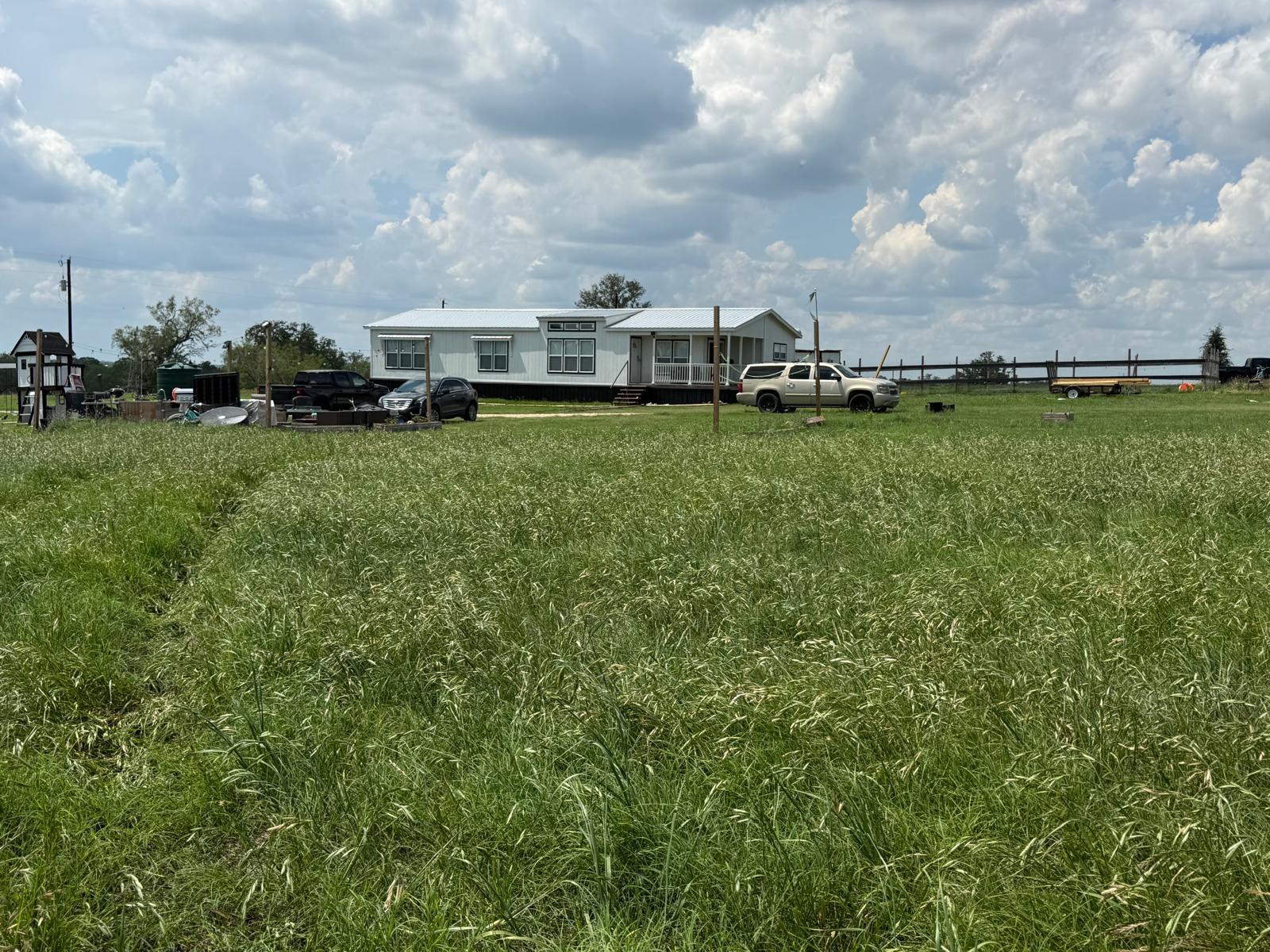 5309 Tenney Creek Road Luling, TX 78648 - Photo 4 of 10 A manufactured home rests amidst a verdant, sprawling yard under an expansive sky.