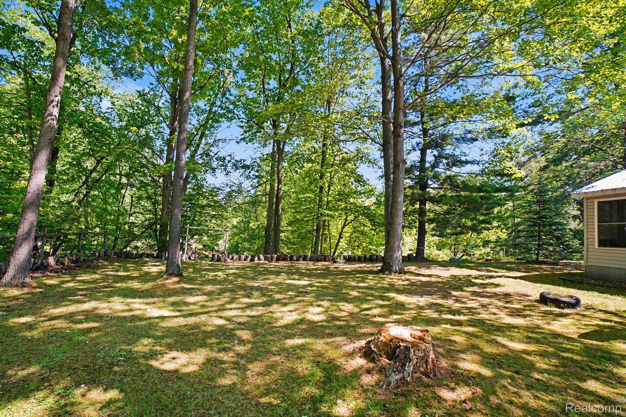 4772 South Bard Road Beaverton, MI 48612 - Photo 37 of 46 Expansive grassy yard with mature trees and a stone retaining wall