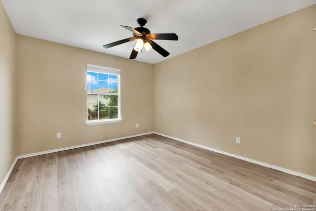 an empty room with wooden floor chandelier fan and windows