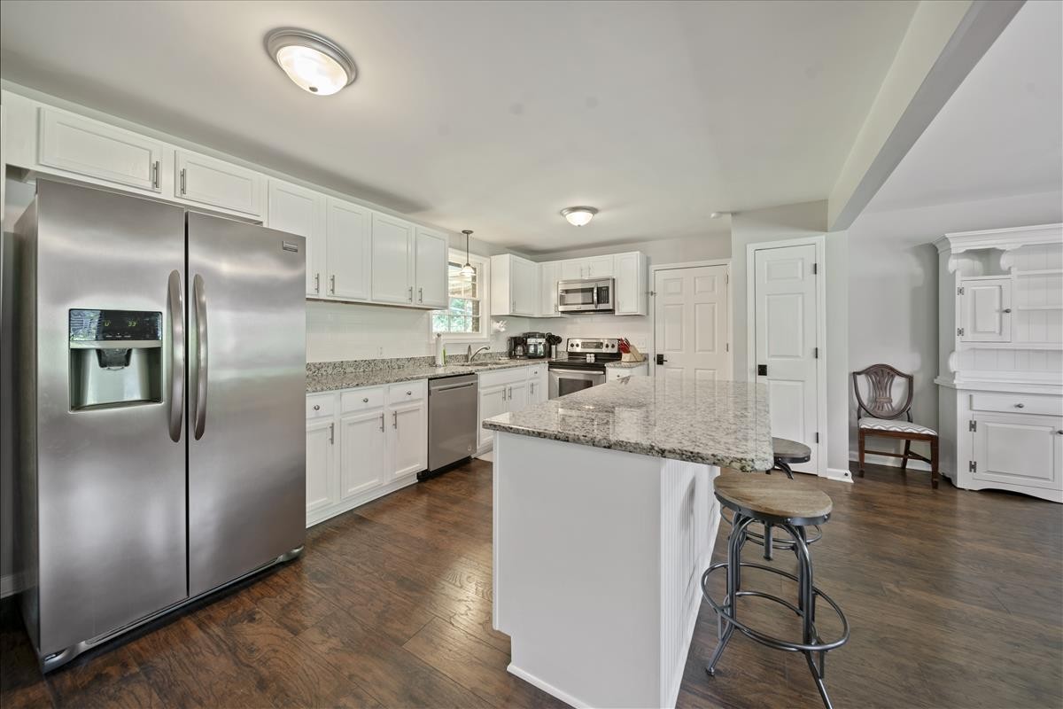 a kitchen with stainless steel appliances kitchen island granite countertop a refrigerator a stove a sink and white cabinets with wooden floor