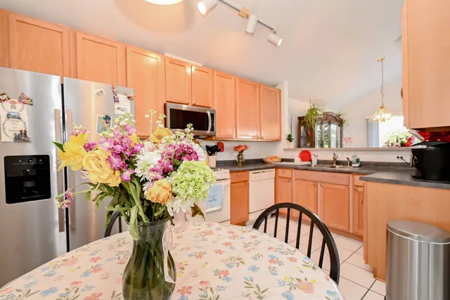 a kitchen with stainless steel appliances kitchen island granite countertop a refrigerator a sink a dining table and chairs with wooden floor