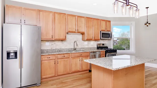 a kitchen with kitchen island granite countertop a stove top oven a sink dishwasher and a refrigerator with wooden floor