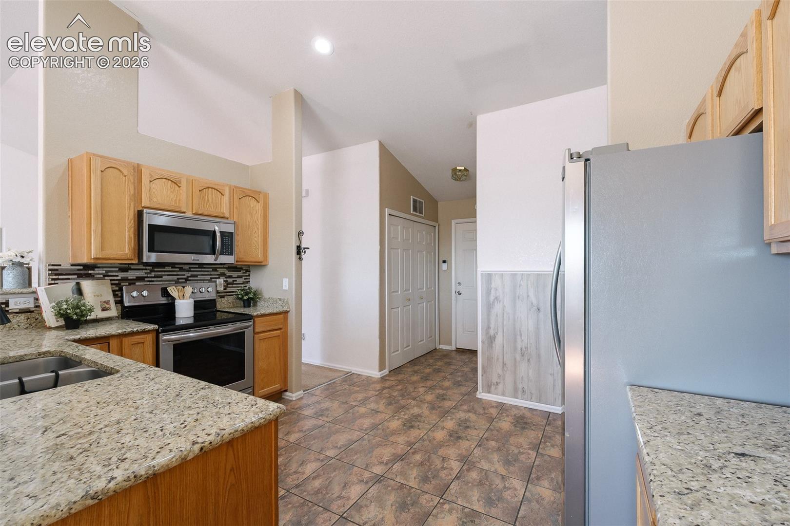 7869 Fort Smith Road Peyton, CO 80831 - Photo 18 of 50 Open and functional kitchen featuring granite countertops, stainless steel appliances, abundant cabinet space, and vaulted ceilings.