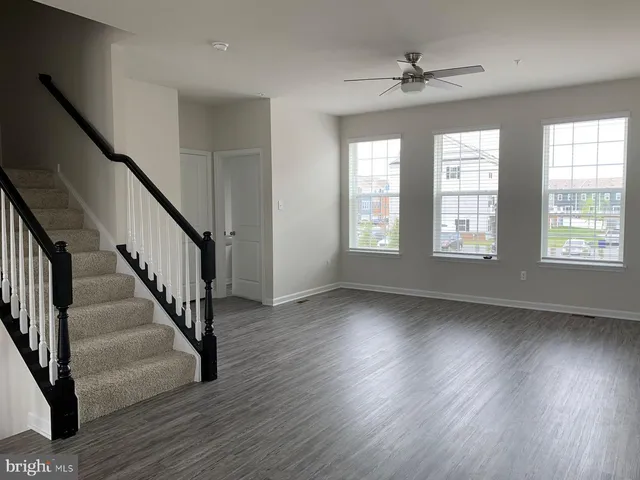 a view of an empty room with wooden floor and fan