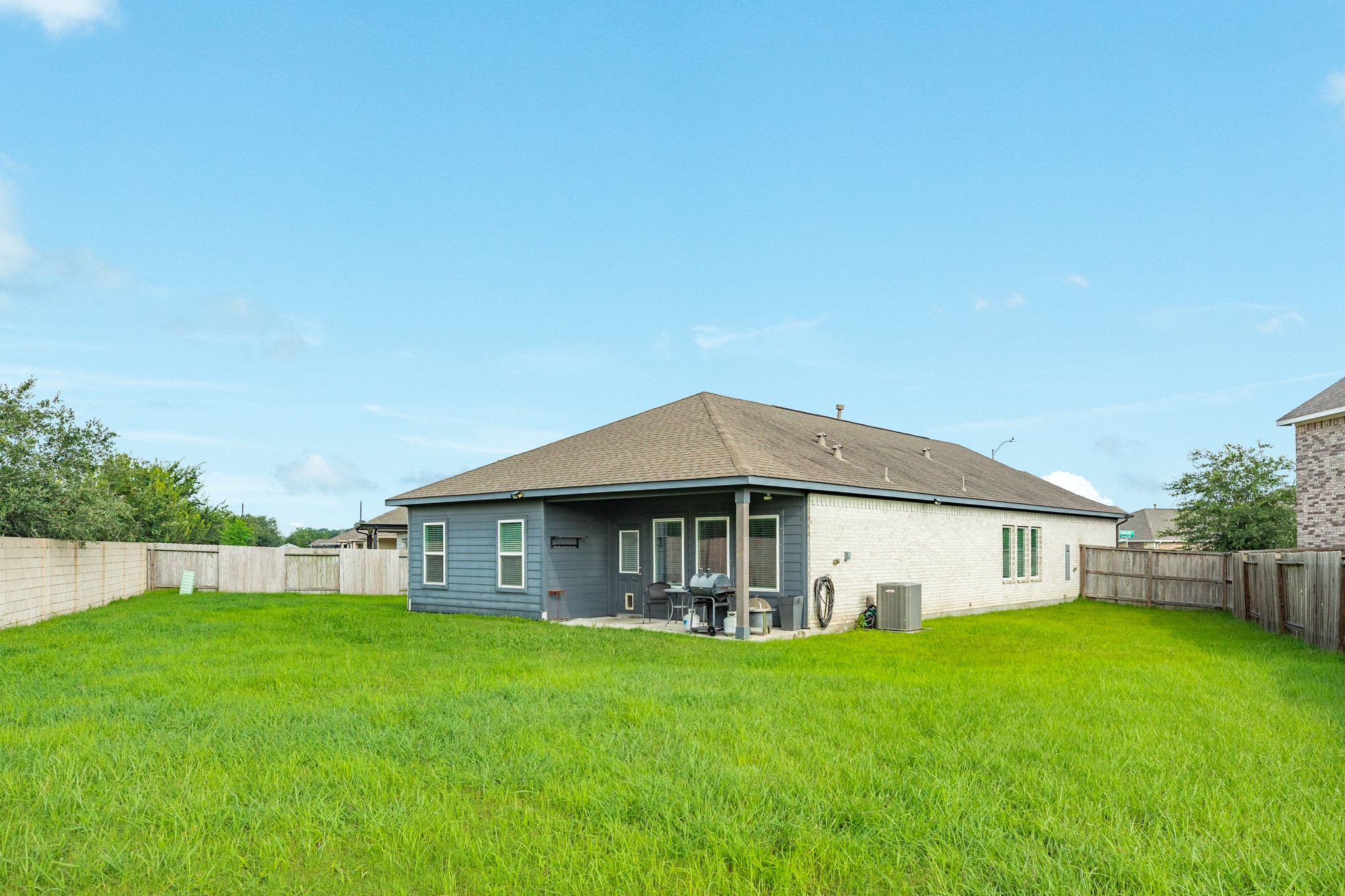 2446 Palisade Crst Drive Rosharon, TX 77583 - Photo 25 of 30 Spacious backyard with a well-maintained lawn, featuring a single-story home with a combination of brick and siding exterior. There's a covered patio area, fenced for privacy, ideal for outdoor activities.