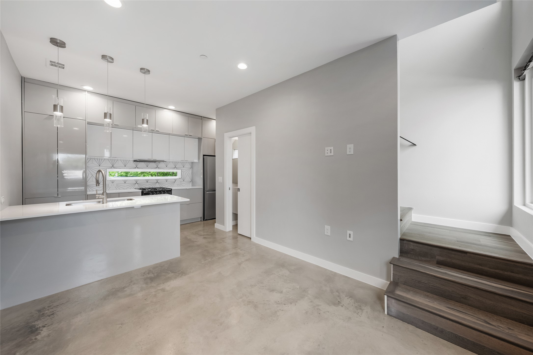 2108 Tillery Street, Unit 16 Austin, TX 78723 - Photo 1 of 15 Contemporary kitchen featuring high-gloss cabinetry, a central island with a sink, a geometric tile backsplash, and stainless steel appliances