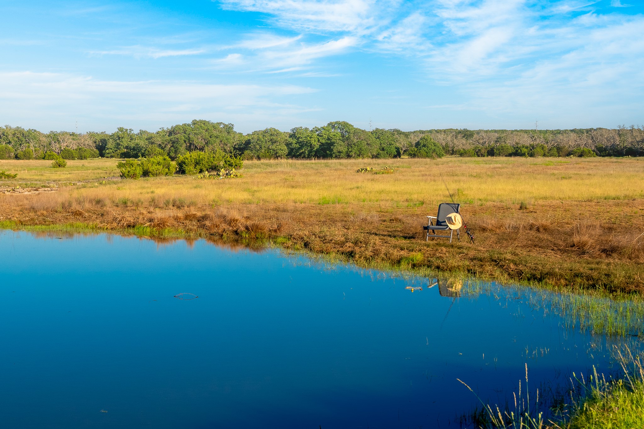 32 Feild Ranch Road Burnet, TX 78611 - Photo 35 of 40 Reflecting the clear blue sky, a tranquil pond awaits amidst a verdant landscape.