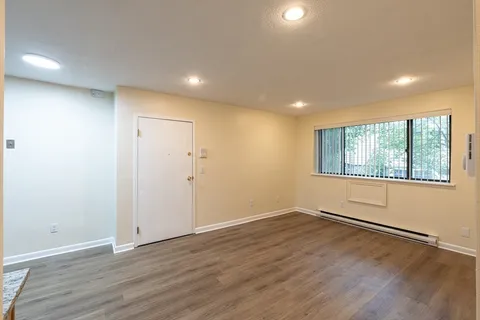 a view of an empty room with wooden floor and a window