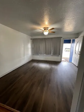 an empty room with wooden floor chandelier fan and windows