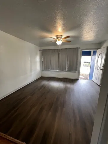 an empty room with wooden floor chandelier fan and windows