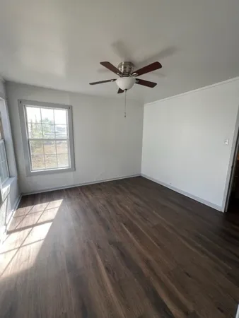 an empty room with wooden floor fan and windows