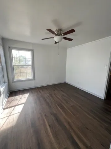 an empty room with wooden floor fan and windows