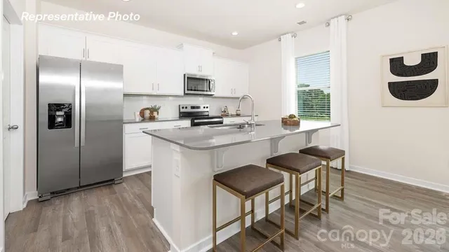 a kitchen with stainless steel appliances a refrigerator a stove a sink and white cabinets with wooden floor