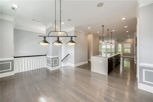 a room with stainless steel appliances kitchen island granite countertop a stove a refrigerator a sink a dining table and chairs with wooden floor