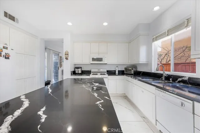 a large white kitchen with granite countertop a sink a stove a refrigerator a washer and dryer with wooden floor