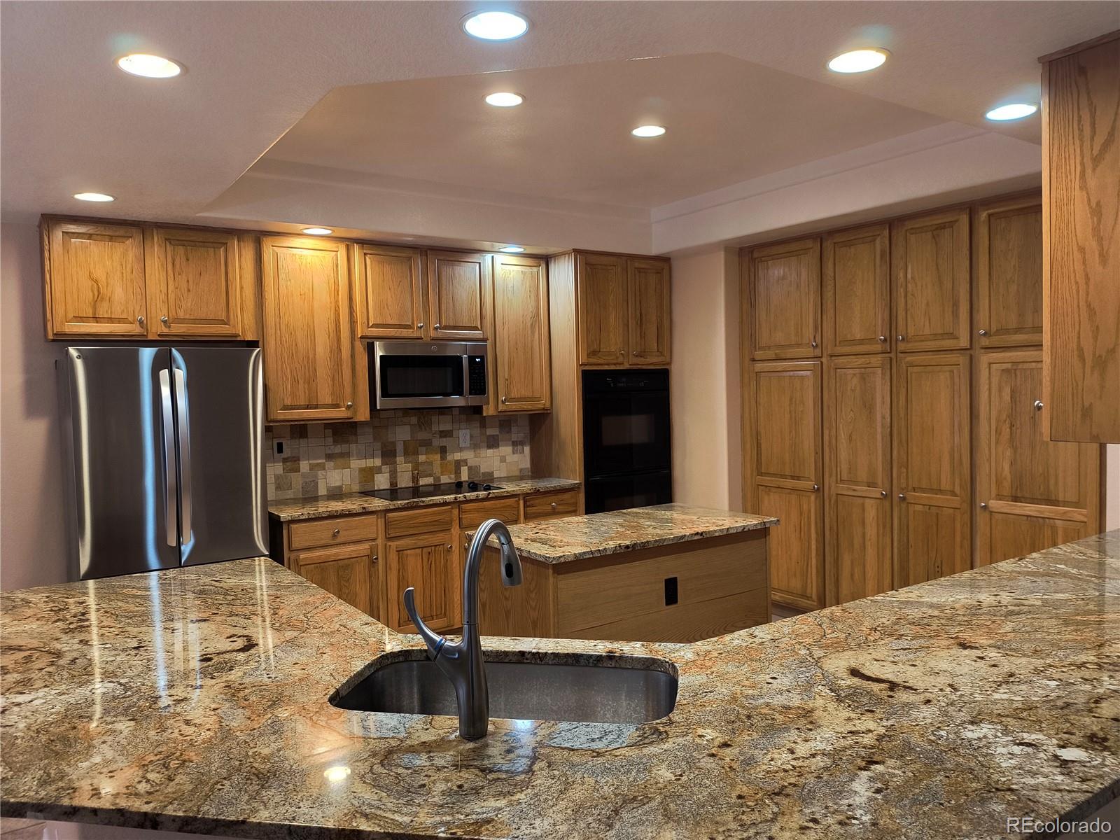 10145 Charissglen Lane Highlands Ranch, CO 80126 - Photo 6 of 39 a kitchen with stainless steel appliances kitchen island granite countertop a refrigerator a stove and a sink with wooden floor