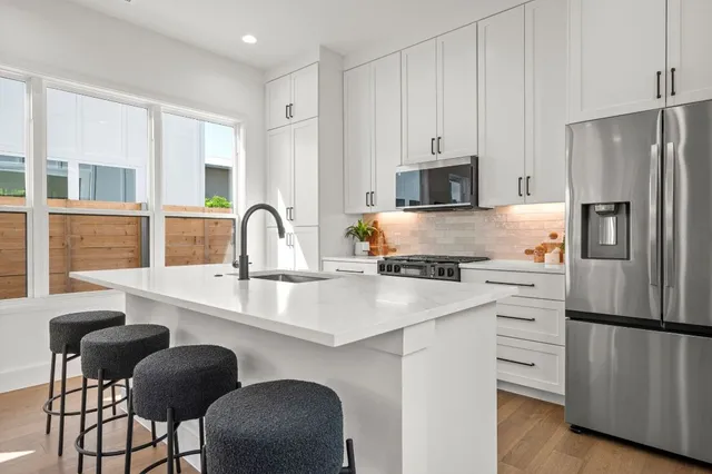 a kitchen with stainless steel appliances granite countertop a stove a sink a refrigerator and white cabinets with wooden floor