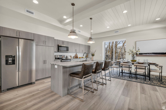 4016 South Burch Way Ogden, UT 84405 - Photo 8 of 30 Modern kitchen featuring wood-finish flooring, stainless steel appliances, an island with countertop seating, recessed lighting, and a white plank ceiling
