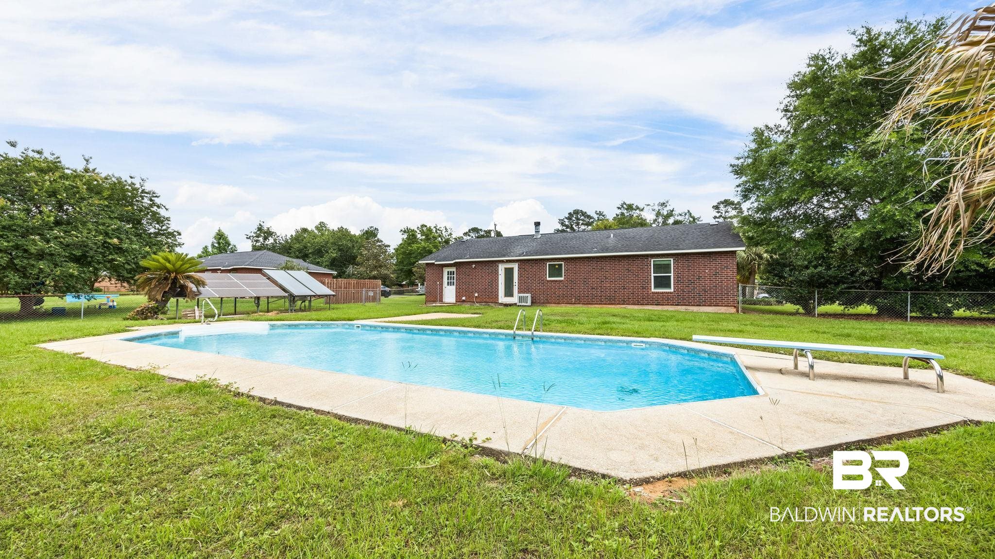 15096 Highland Circle Foley, AL 36535 - Photo 51 of 52 Spacious backyard featuring an in-ground swimming pool with concrete surround and diving board, a brick exterior home, mature trees, and solar panels