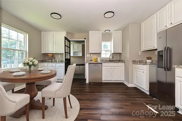 a kitchen with stainless steel appliances kitchen island granite countertop a dining table chairs and a refrigerator