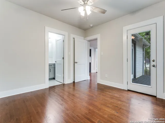 a view of an empty room with wooden floor and a ceiling fan