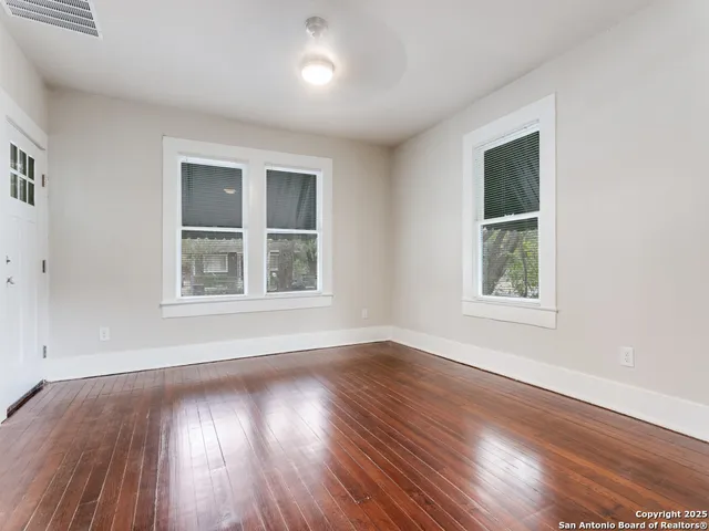a view of an empty room with wooden floor and a window