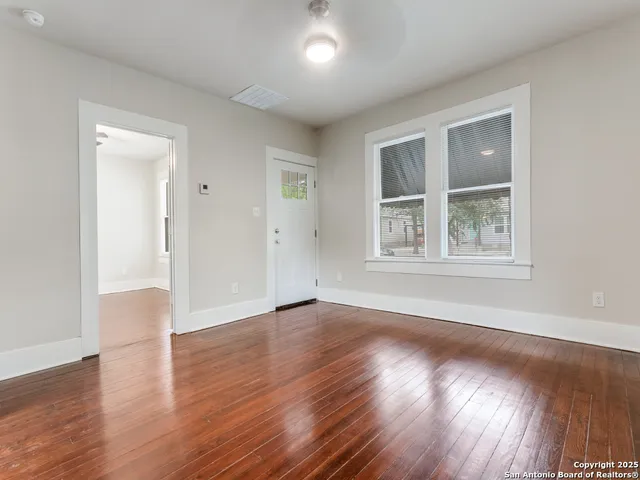 a view of an empty room with wooden floor and a window