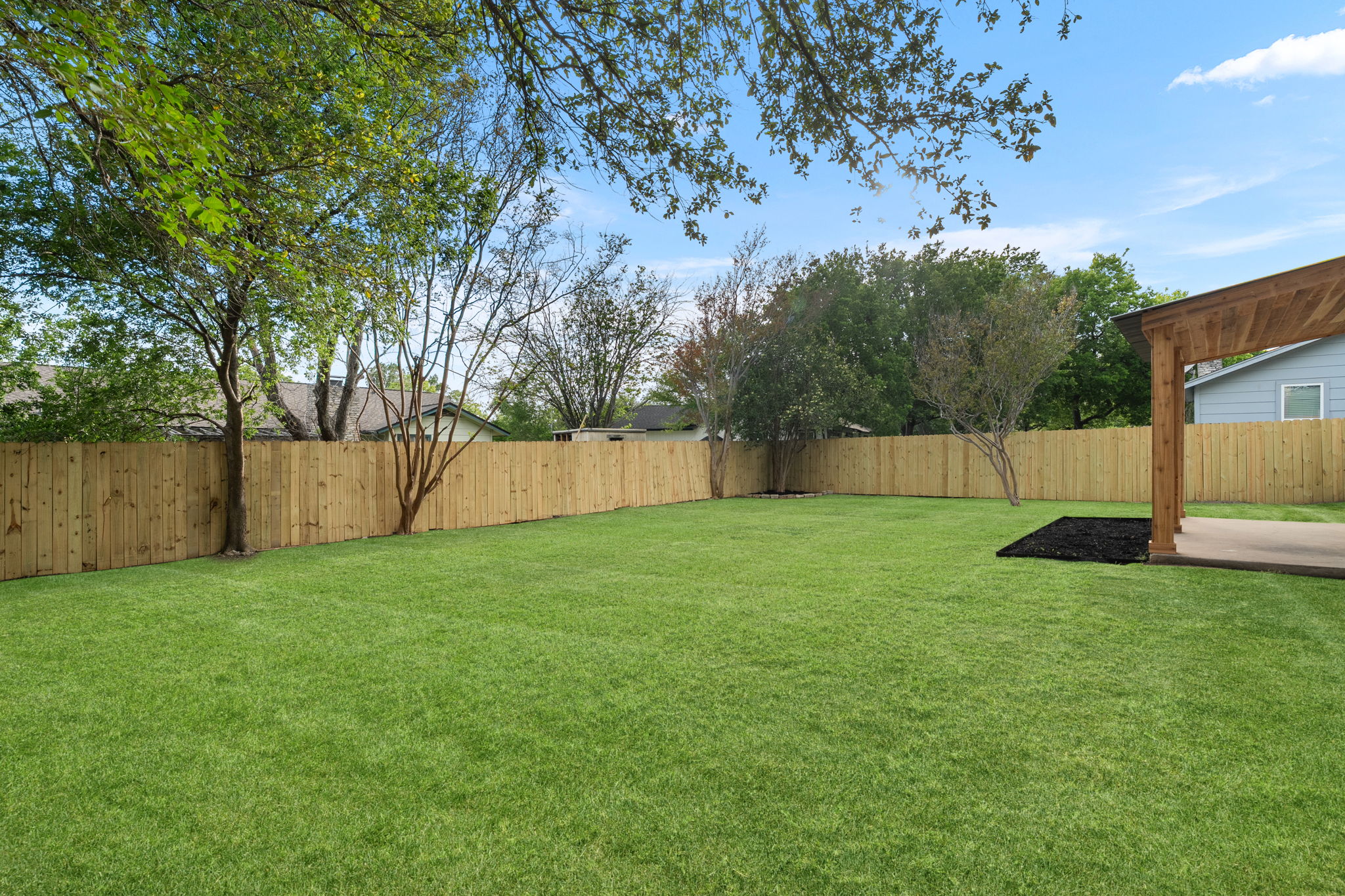 2107 Cindy Lane Austin, TX 78727 - Photo 30 of 33 Expansive backyard featuring a new wood privacy fence, mature trees, a concrete patio, and a wood-beamed pergola