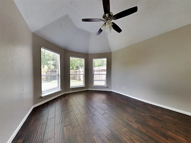 an empty room with wooden floor fan and windows