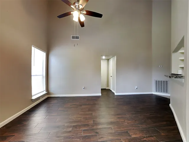 an empty room with wooden floor fan and windows