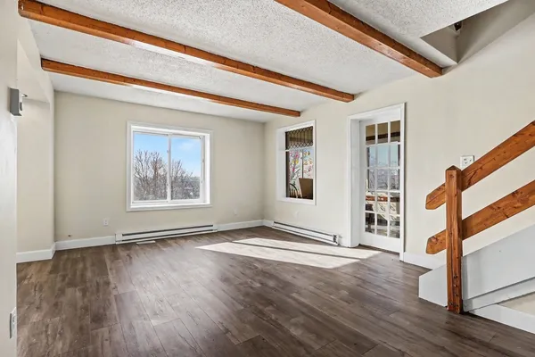 a view of an empty room with wooden floor and a window