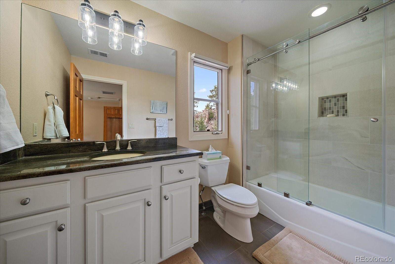6737 Timbers Drive Evergreen, CO 80439 - Photo 30 of 47 a bathroom with a granite countertop toilet a sink a mirror a bathtub and shower