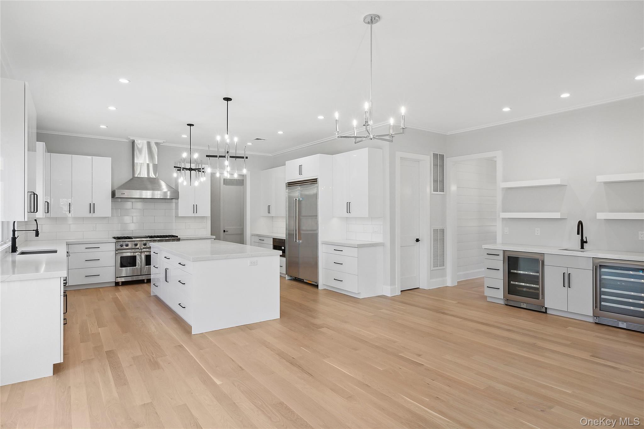 34 Old Main Road Quogue, NY 11959 - Photo 6 of 16 a large white kitchen with kitchen island a stove a sink dishwasher and a refrigerator with wooden floor