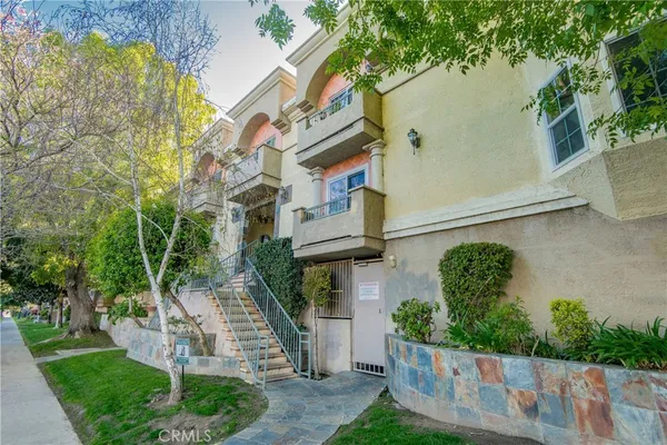 a view of a brick house with a small yard plants and a large tree