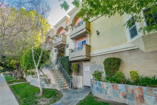 a view of a brick house with a small yard plants and a large tree