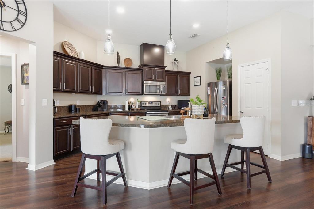 656 Carya Court DeLand, FL 32724 - Photo 8 of 28 a kitchen with stainless steel appliances granite countertop a stove a refrigerator a kitchen island a dining table and chairs with wooden floor