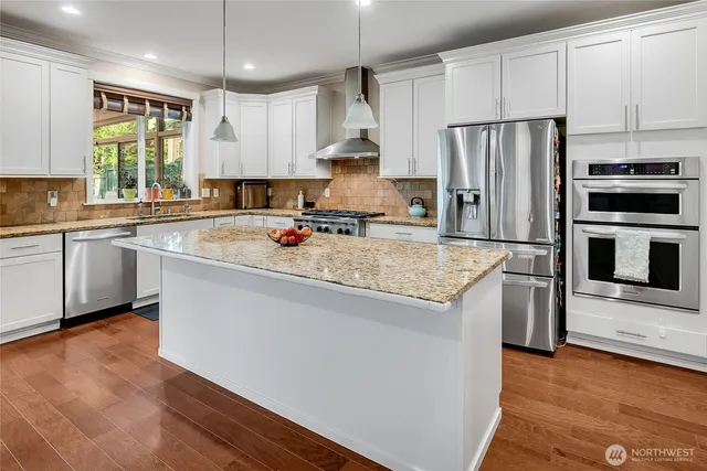 a kitchen with stainless steel appliances granite countertop a sink a stove a refrigerator and island with wooden floor