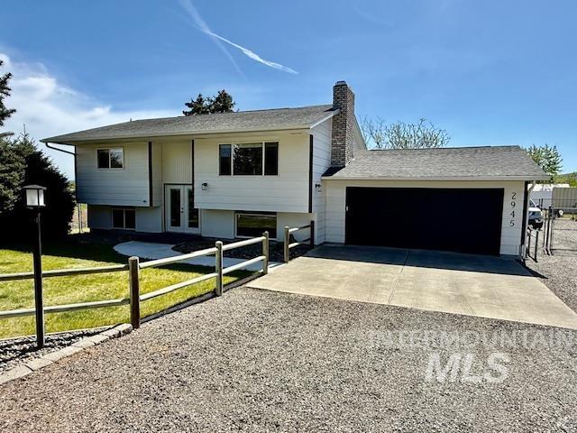 Raised ranch with driveway, a chimney, french doors, and a shingled roof