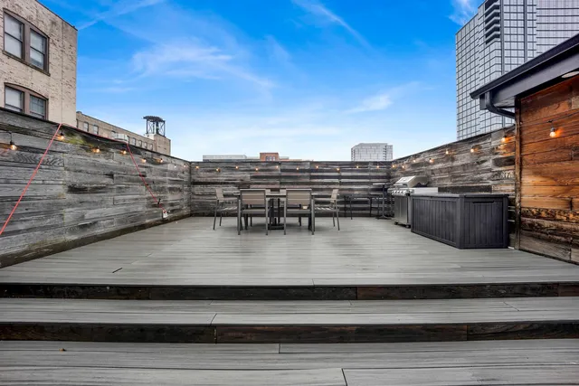 a view of a roof deck with table and chairs a barbeque with wooden floor and city view