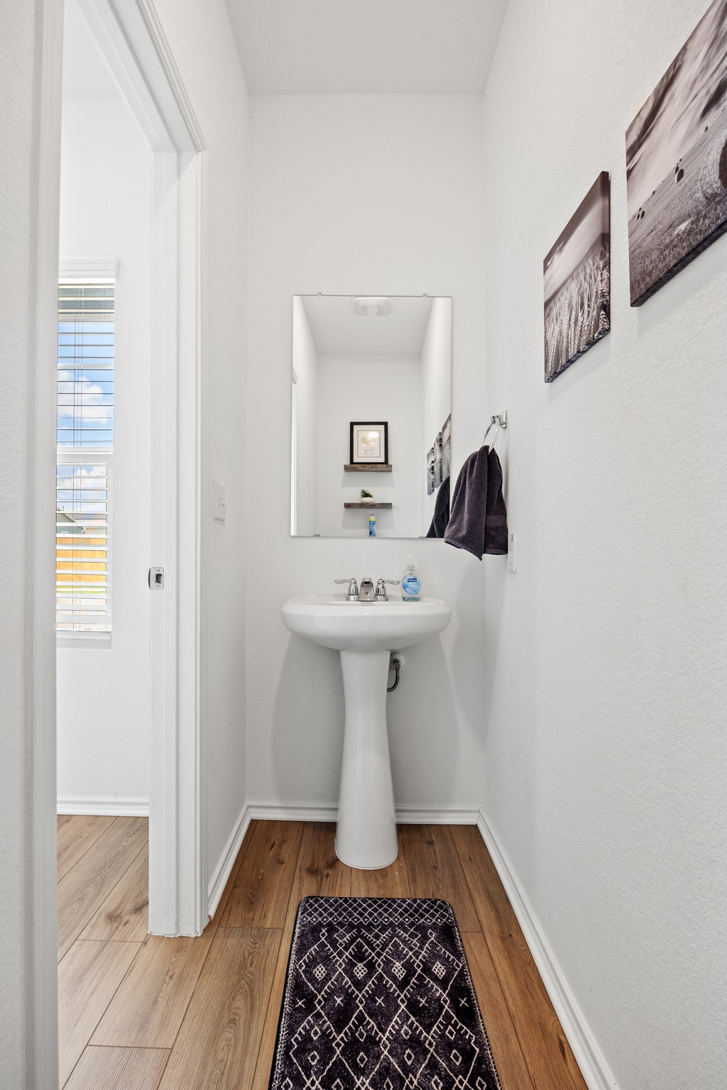 14121 Berning Road Manor, TX 78653 - Photo 14 of 27 A well-appointed half bath features wood-look flooring and a classic pedestal sink, offering functional elegance.