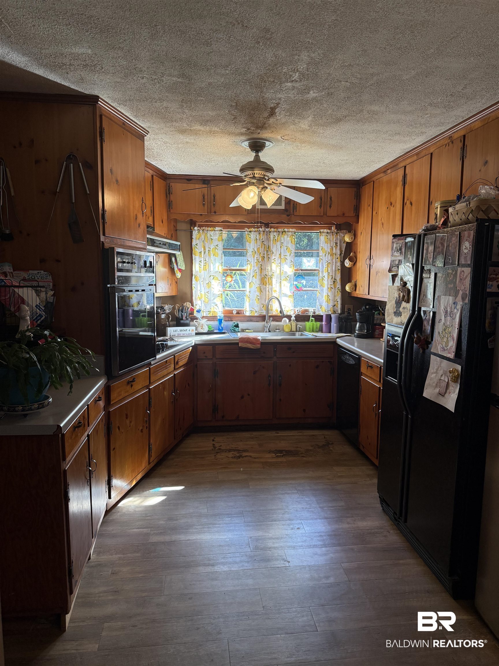 22173 1st Street Silverhill, AL 36576 - Photo 6 of 16 Kitchen with black appliances, a textured ceiling, dark wood-style floors, light countertops, and brown cabinets