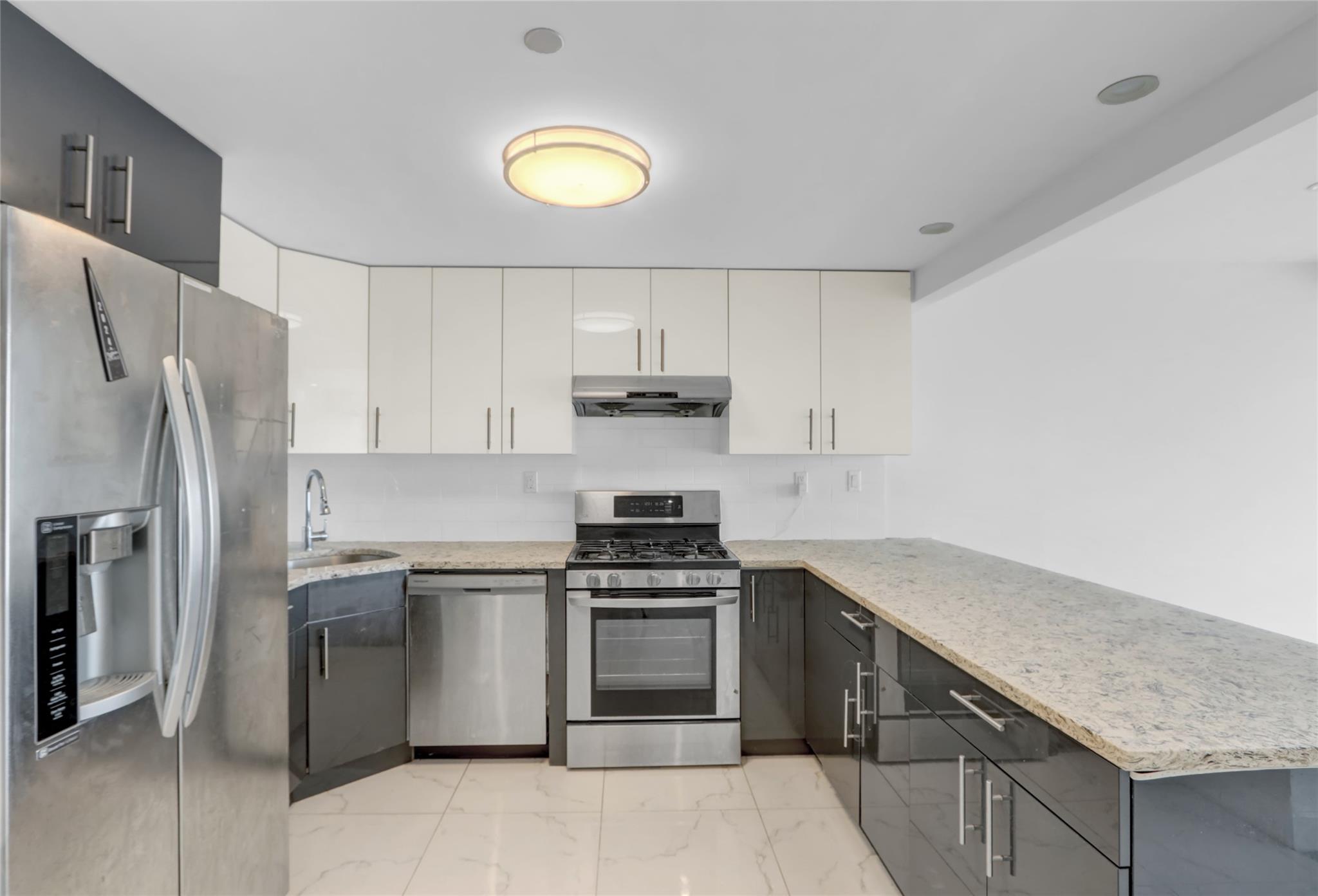 45-16 83rd Street, Unit E6J Queens, NY 11373 - Photo 3 of 19 Kitchen featuring a peninsula, appliances with stainless steel finishes, marble finish floor, light stone counters, and under cabinet range hood