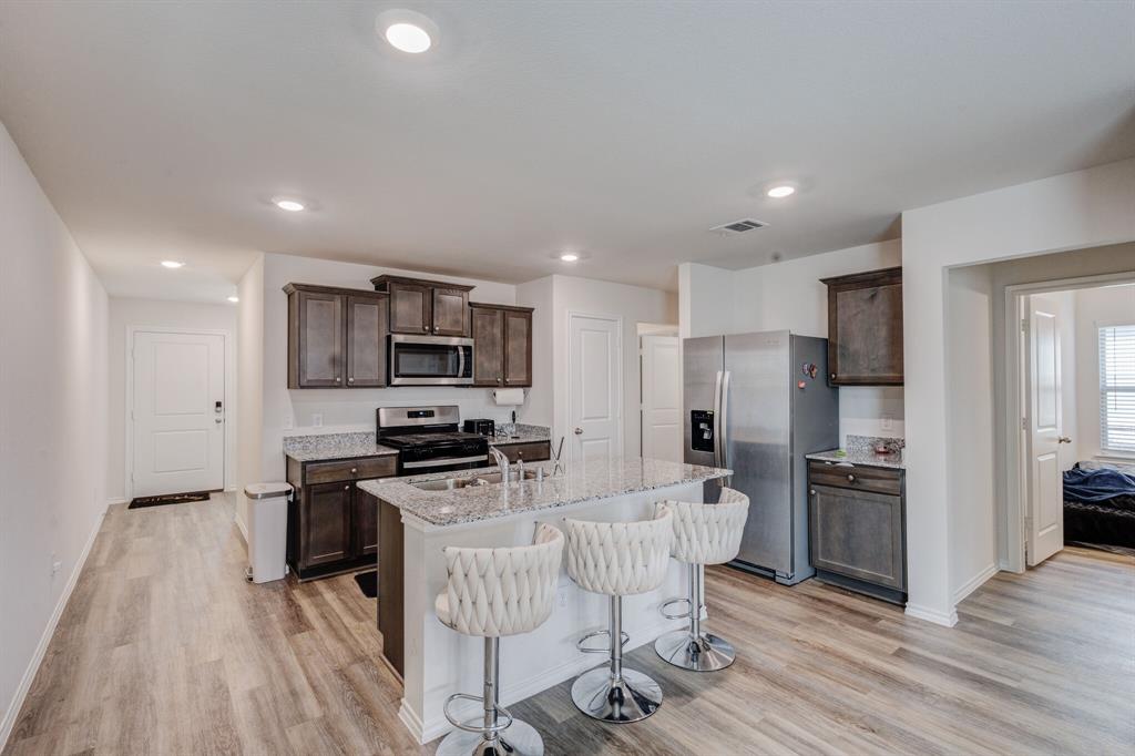 806 Ramble Road Lavon, TX 75166 - Photo 8 of 24 a kitchen with stainless steel appliances a microwave a stove a sink dishwasher a refrigerator and white cabinets with wooden floor