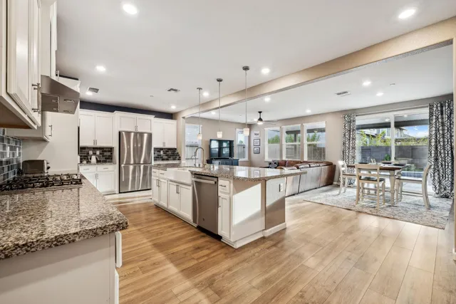 a kitchen with stainless steel appliances kitchen island granite countertop a refrigerator a stove a sink and white cabinets with wooden floor