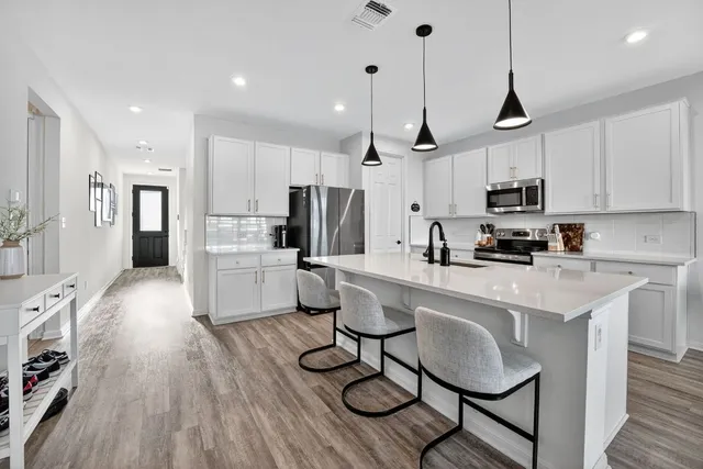 a kitchen with stainless steel appliances a refrigerator a stove a sink and white cabinets with wooden floor