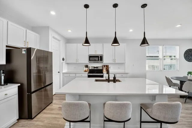 a kitchen with stainless steel appliances granite countertop a sink a refrigerator a stove a kitchen island a dining table and chairs