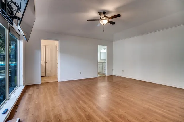 an empty room with wooden floor chandelier fan and windows