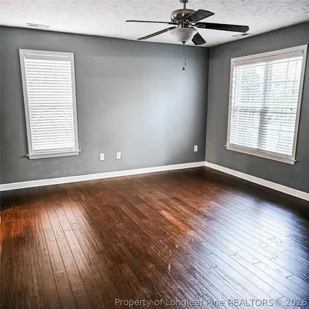 an empty room with wooden floor chandelier fan and windows