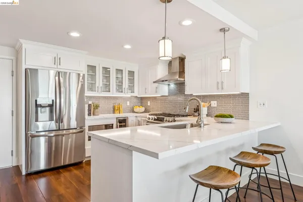 a kitchen with stainless steel appliances granite countertop a refrigerator a sink dishwasher a stove and white cabinets with wooden floor