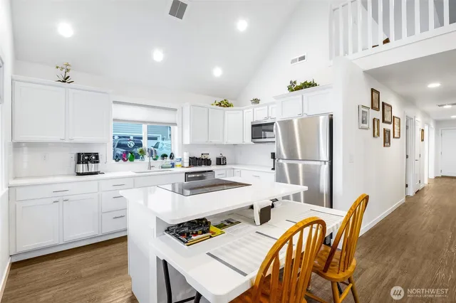 a kitchen with stainless steel appliances a refrigerator a stove a sink dishwasher a dining table and chairs with wooden floor